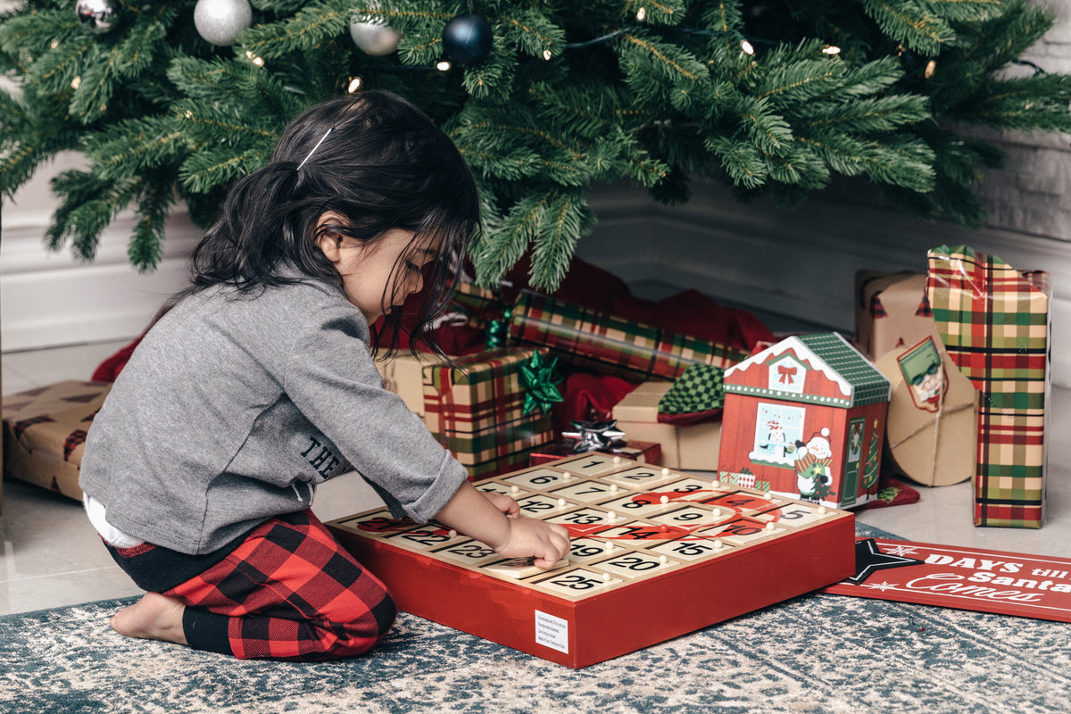 Child opening an Advent calendar under a Christmas tree
